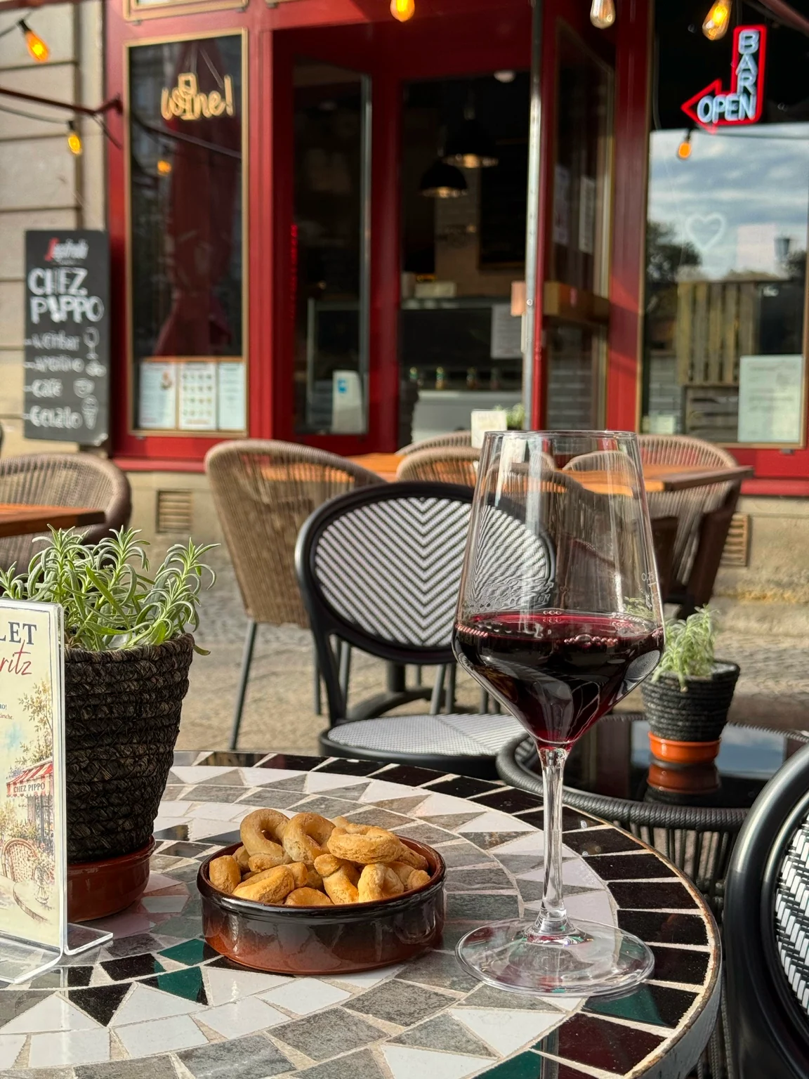 Glas Rotwein und Knabbereien auf einem kleinen Mosaiktisch auf der Terrasse von CHEZ P!PPO