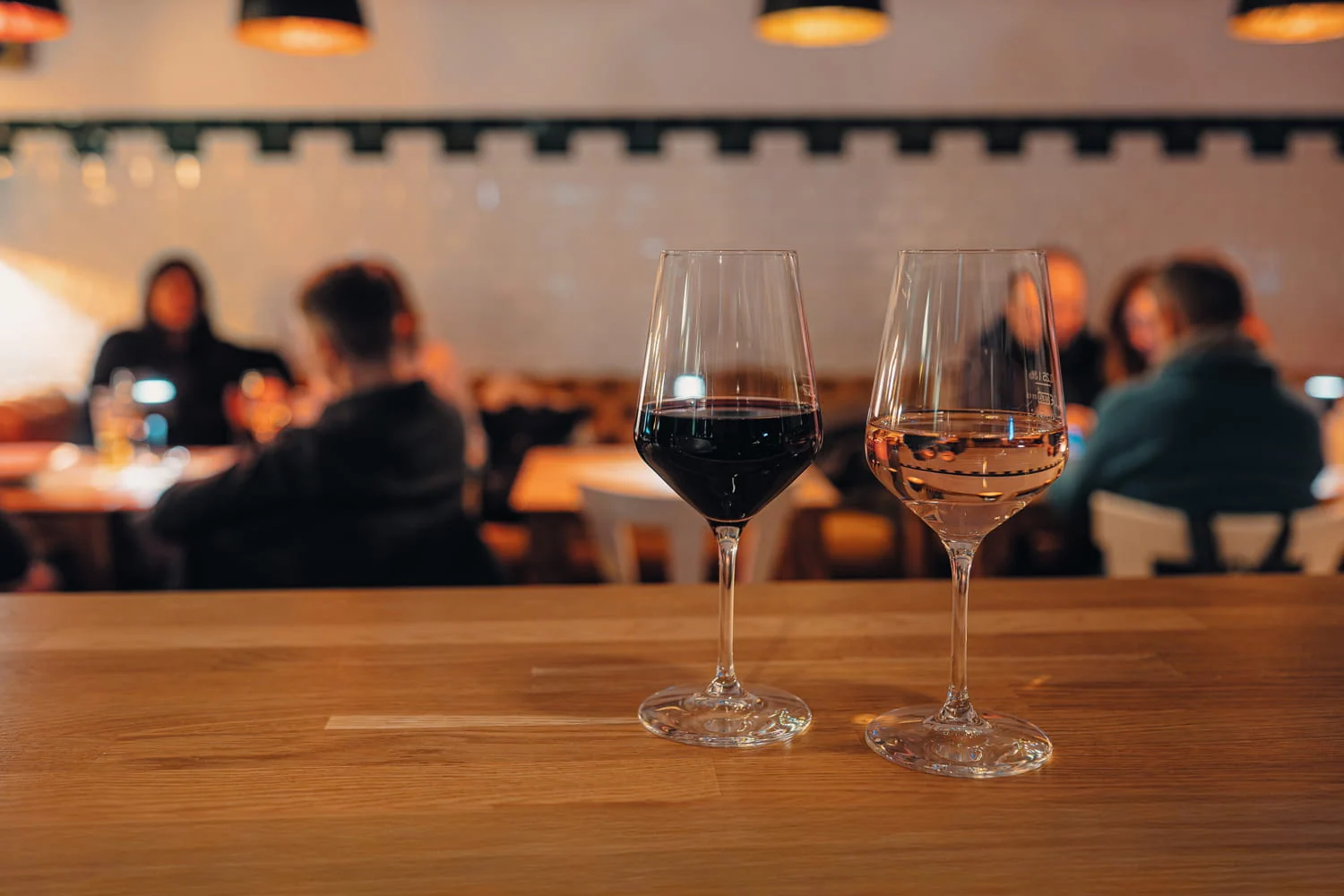 Ein Glas Rotwein und ein Glas Weißwein auf dem Tresen mit Gästen im Hintergrund