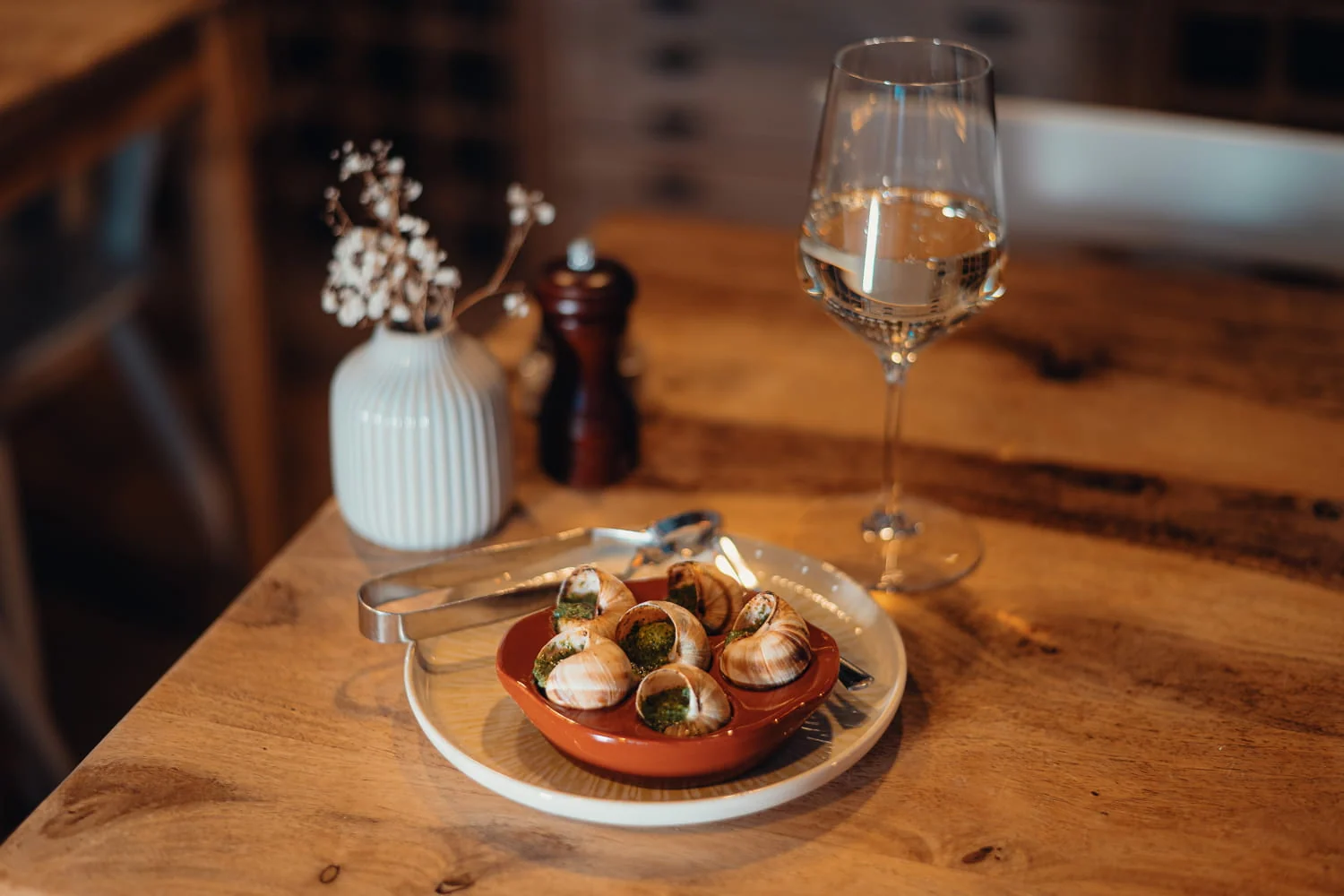 Escargots und ein Glas Weißwein auf einem gedeckten Holztisch