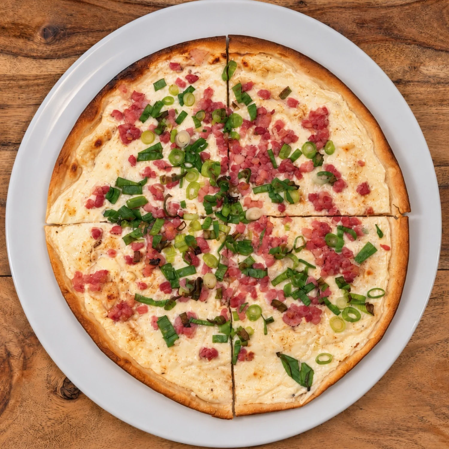 Flammkuchen mit Crème fraîche, Speck und Frühlingszwiebeln auf weißem Teller