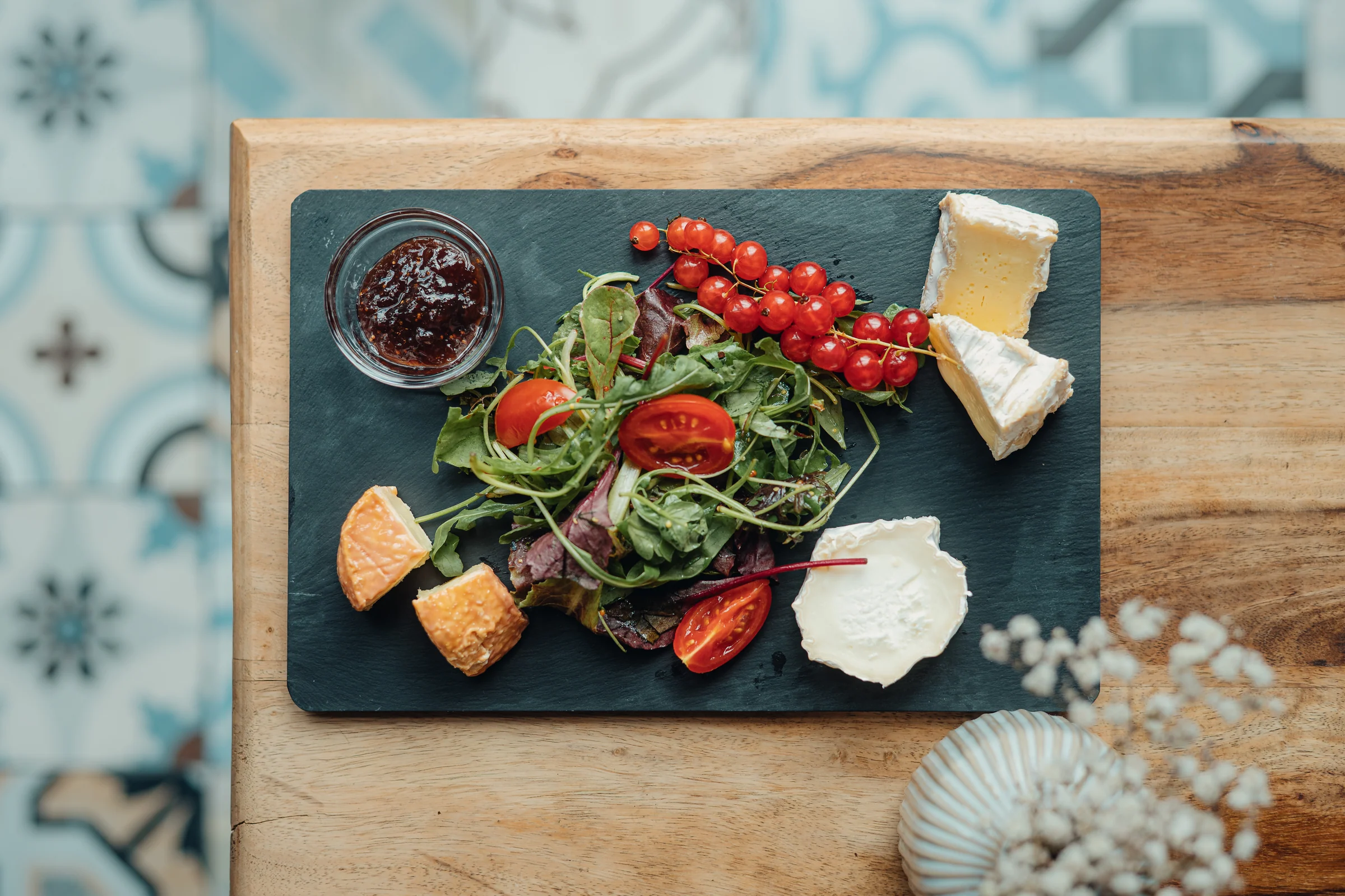 Französische Käseauswahl mit Salat, Johannisbeeren und Konfitüre auf einer Schieferplatte